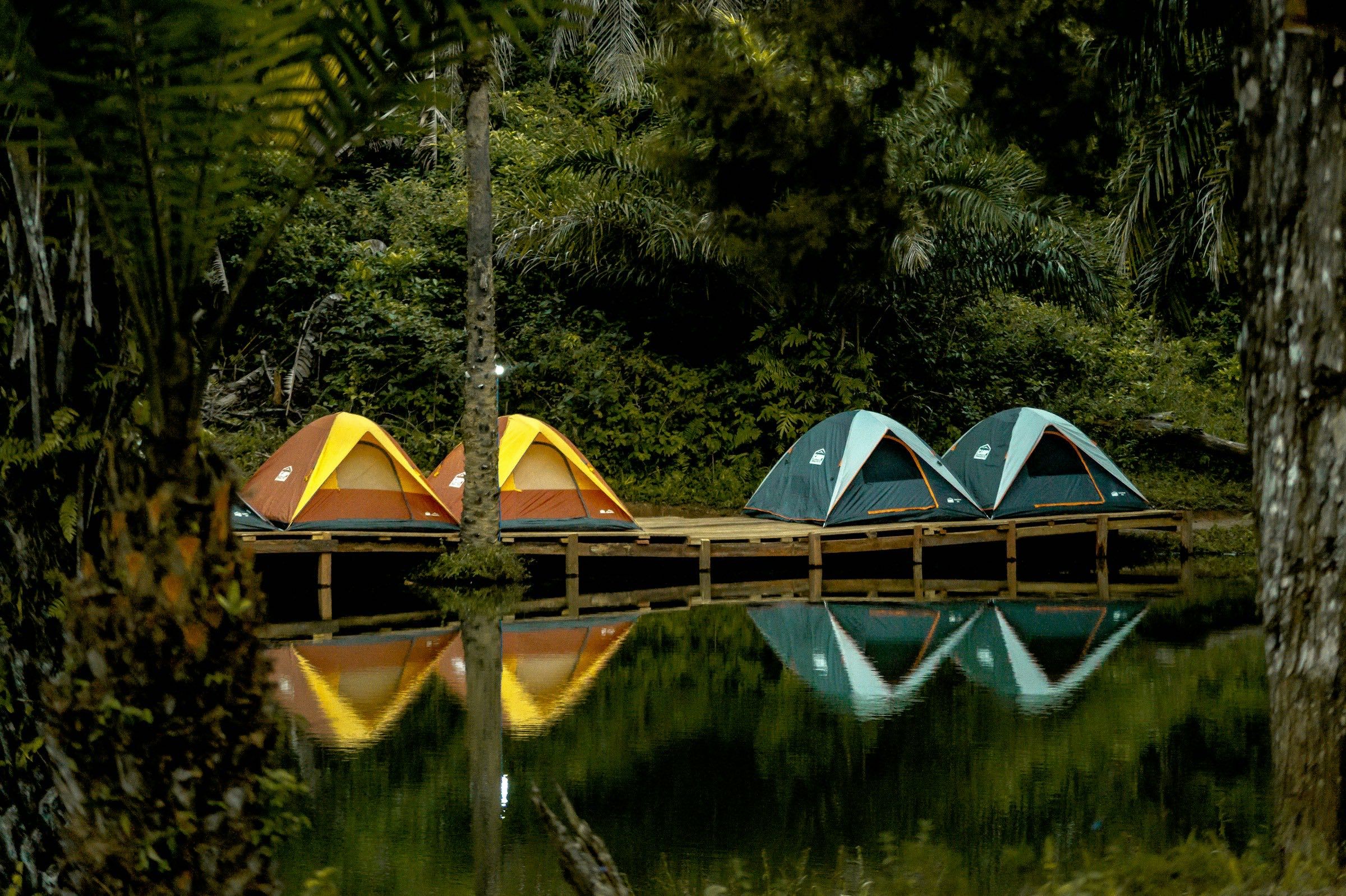 Yellow and teal dome tents on a wooden jetty reflected in a still lake