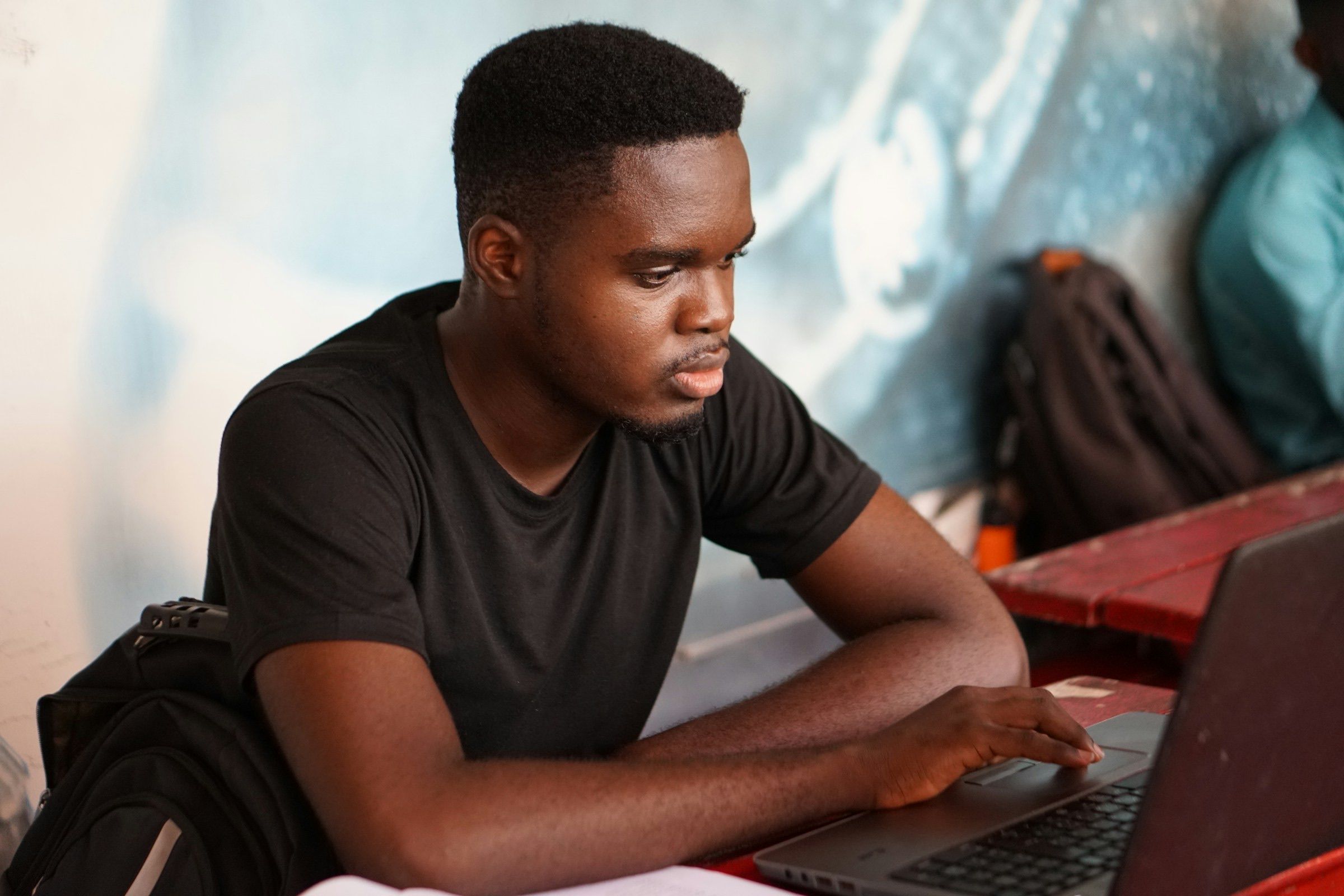 Young man in a plain grey t-shirt working on a laptop at a table