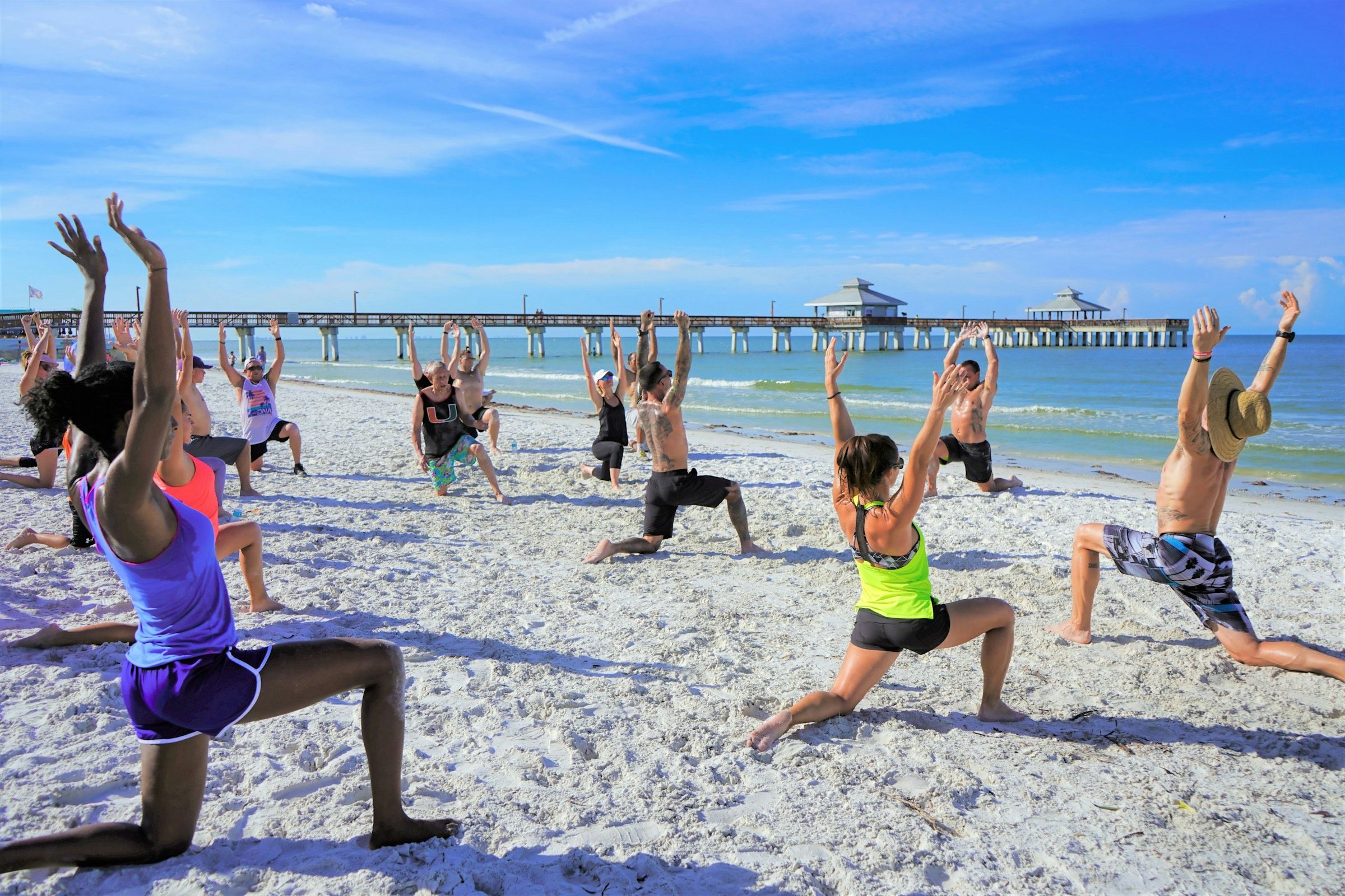 Group doing lunges and stretches in an outdoor fitness class on a sandy beach