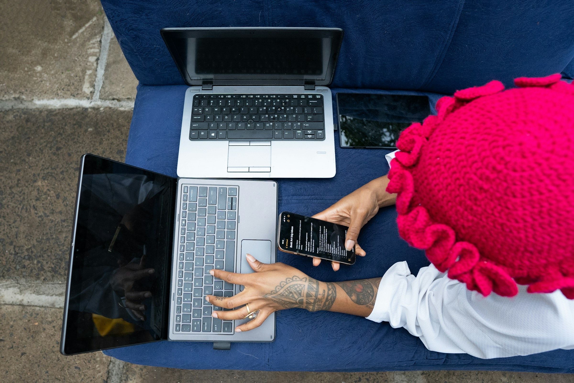 Overhead view of a person working on two laptops and a phone on a blue couch