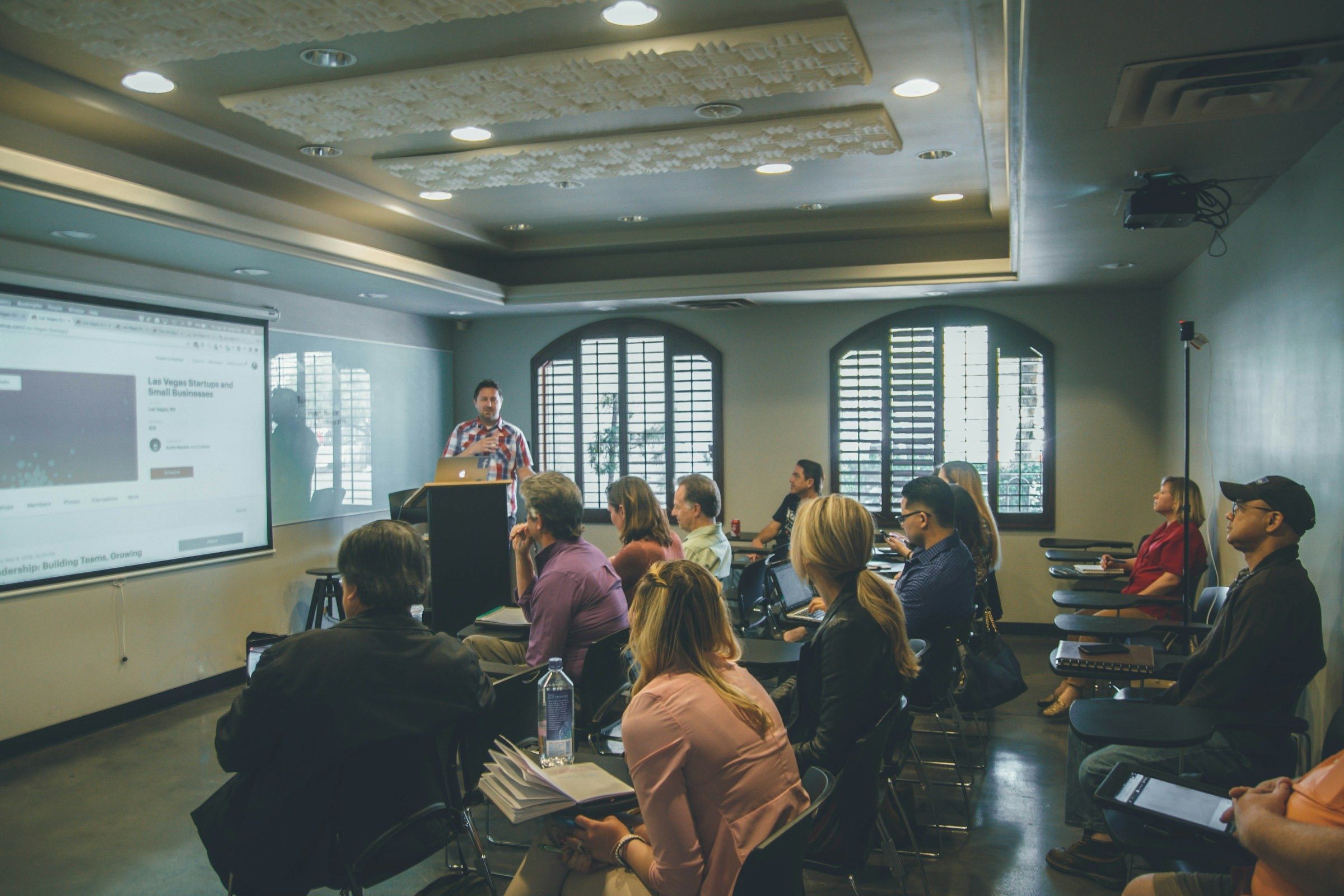 Audience watching a presenter beside a projector screen in a seminar room
