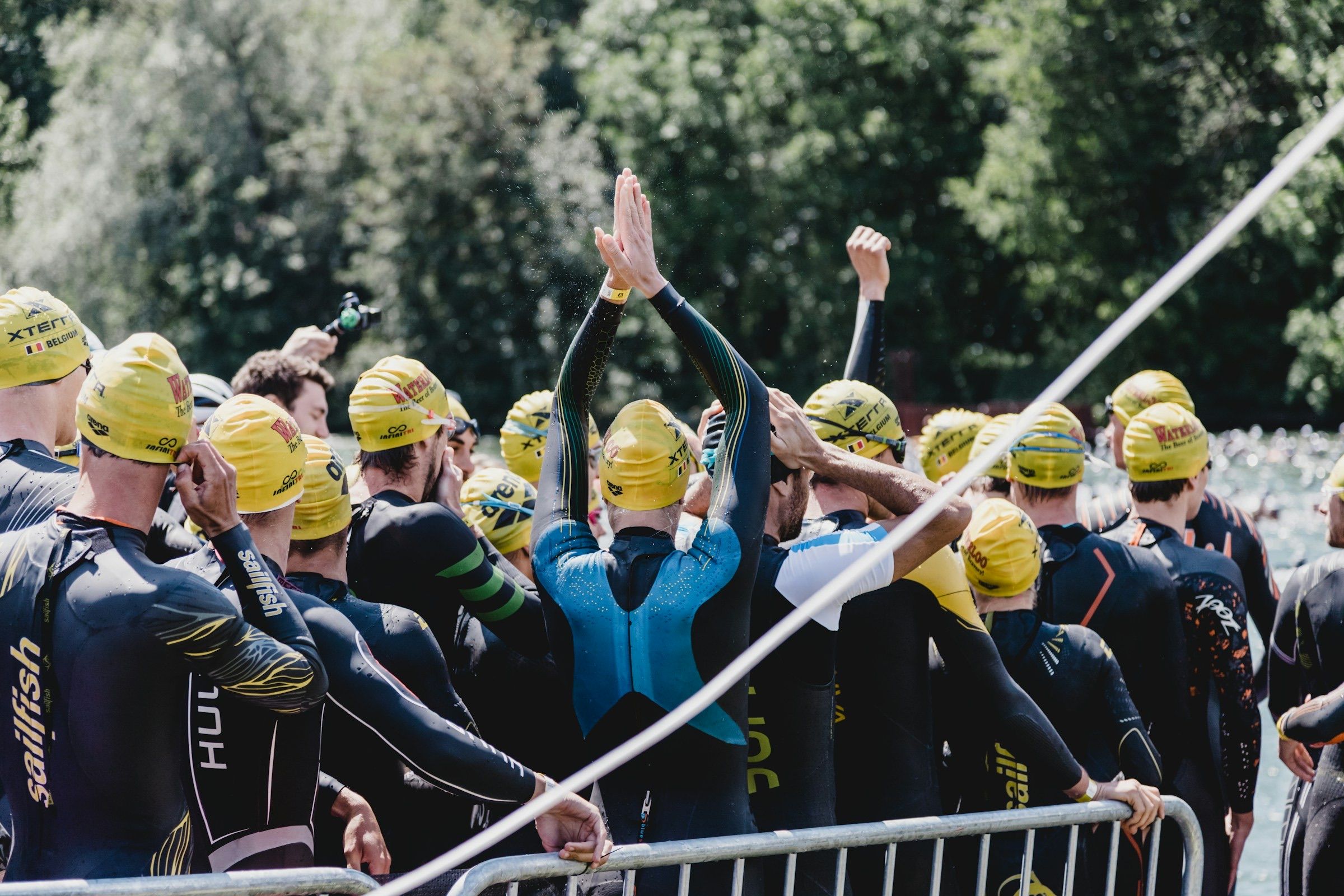 Triathletes in wetsuits and yellow caps gathered at a swim start