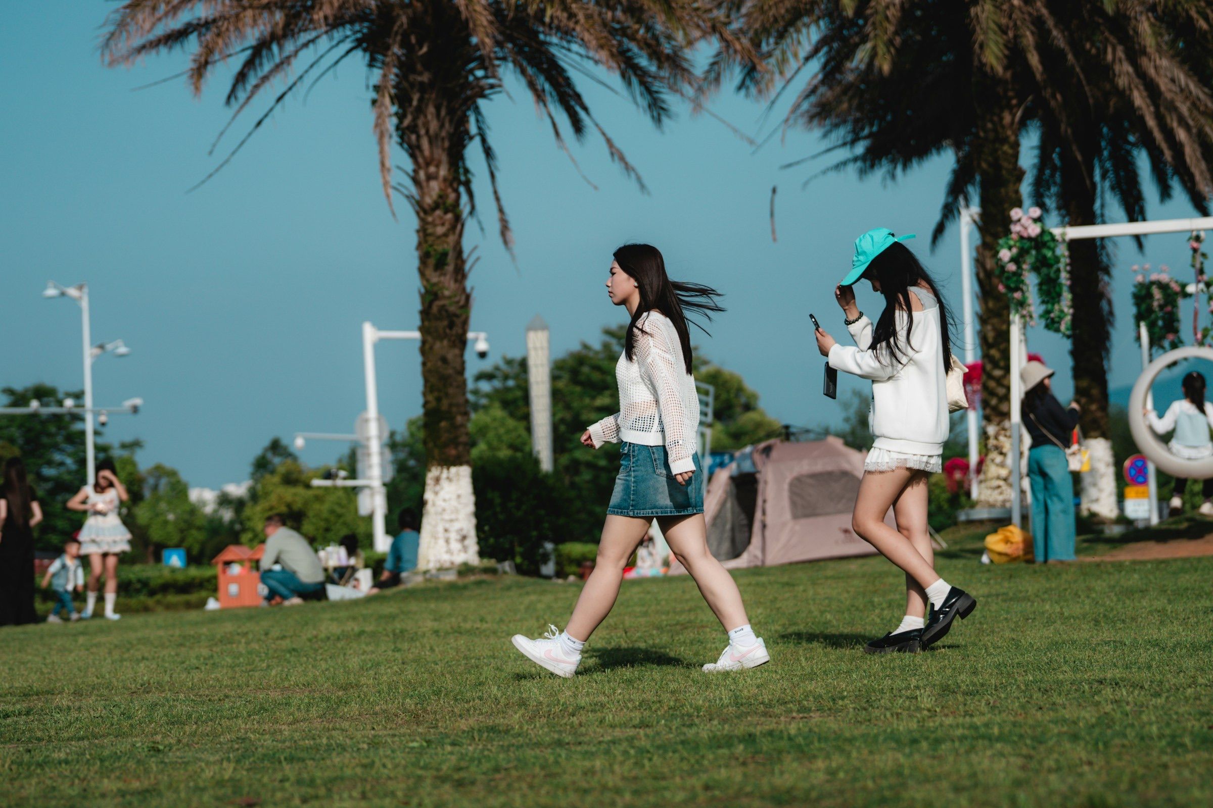 Two young women walking across a sunny lawn beside palm trees