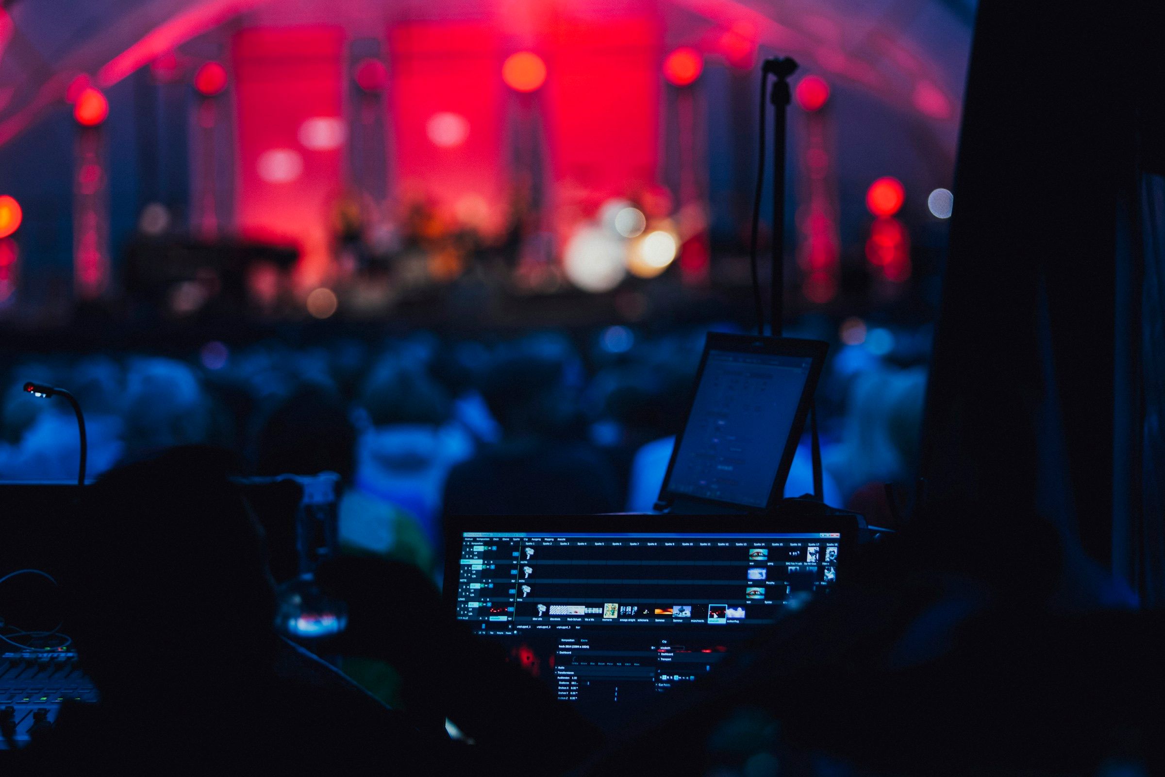 Production desk with a monitor and laptop facing a lit stage and audience